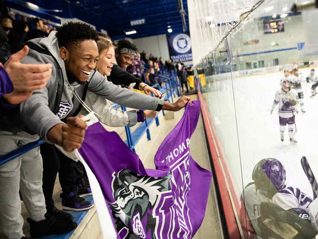 Students at a hockey game lean forward with a purple St Ҵý flag